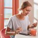 Smiling woman savoring a fresh breakfast with juice and dessert indoors.